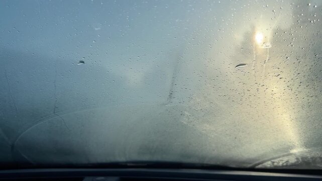 Interior view of a car windshield covered in thick frost and condensation with the morning sun glowing through