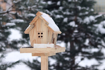 Bird feeder in winter. The feeder looks like a house with a window and a roof. A place for feeding wild birds. A beautiful wooden feeder with seeds and a piece of lard for tits. Winter © Mariia