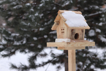 Bird feeder in winter. The feeder looks like a house with a window and a roof. A place for feeding wild birds. A beautiful wooden feeder with seeds and a piece of lard for tits. Winter © Mariia