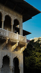 Obraz premium Ornate heritage palace balcony with carved arches and stone detailing in Jaipur, Rajasthan, showcasing traditional Indian architecture under a clear blue sky.