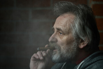 Senior bearded man smoking on balcony classic big cigar in detail