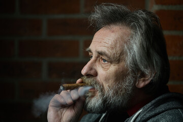 Senior bearded man smoking on balcony classic big cigar in detail