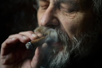 Senior bearded man smoking on balcony classic big cigar in detail