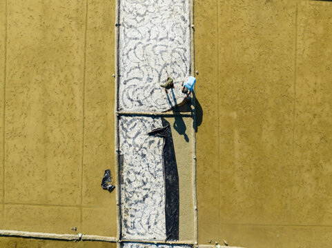Aerial view of a person casting a long shadow as they work on a patterned surface, contrasting against the solid backdrop, Cox's Bazar, Bangladesh.