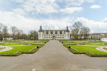 Fototapeta premium A large white building of Neuhaus Castle in Paderborn Germany with a courtyard in front of it. The courtyard is surrounded by a gravel path and has a lot of flowers