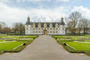 Obraz premium A large white building of Neuhaus Castle in Paderborn Germany with a courtyard in front of it. The courtyard is surrounded by a gravel path and has a lot of flowers