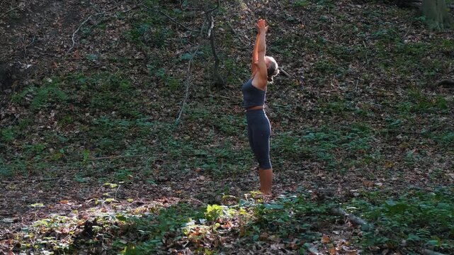 Young woman practicing yoga in the forest, performing standing backbend and forward fold poses in nature, wellness and mindfulness concept.