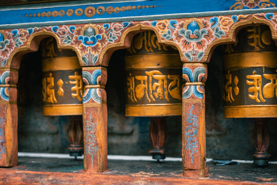 Paro, Bhutan - 16 September 2025: View of intricately carved prayer wheels, their golden surfaces adorned with ancient scripts, nestled beneath a vibrant canopy of floral patterns.