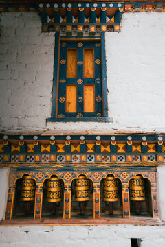 Paro, Bhutan - 16 September 2025: View of intricately decorated window and prayer wheels against a textured white wall, displaying Bhutanese artistry.