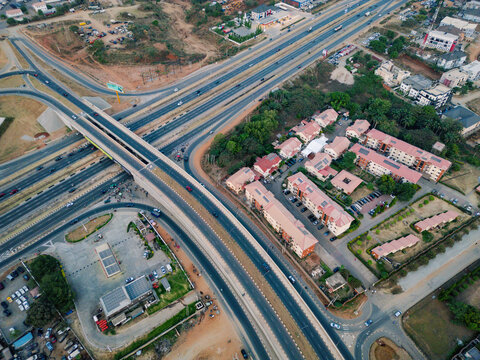 Aerial view of a complex interchange system, with vehicles flowing through multiple lanes, surrounded by residential buildings and lush greenery, Abuja, Federal Capital Territory, Nigeria.