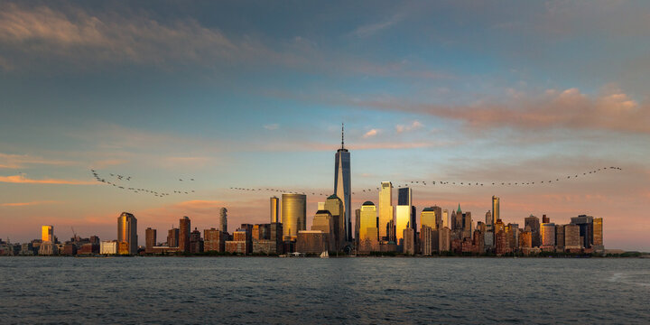 View of the golden light kissing the skyscrapers of the city as birds fly over the waters of the bay in New York City, New York, USA.