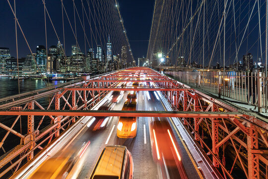 View of blurred car lights streak across the Brooklyn Bridge at night, juxtaposed against the sparkling cityscape of Manhattan, New York City, USA.