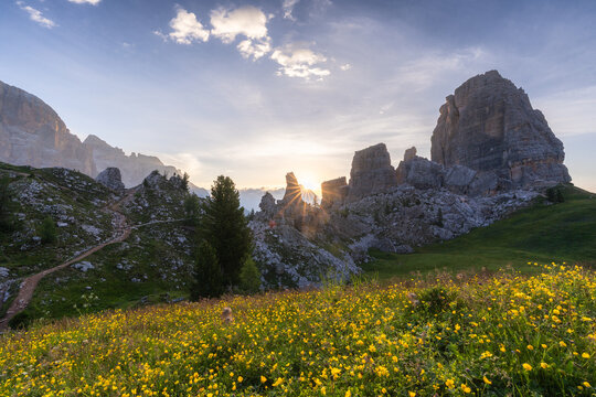 View of sun rays piercing through the majestic Dolomites, illuminating a vibrant meadow of yellow flowers, Cortina d'Ampezzo, Veneto, Italy.