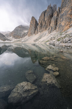 View of jagged peaks reflected in the calm waters of a mountain lake, with rocks visible beneath the surface, in Campitello di Fassa, Trentino-Alto Adige, Italy.