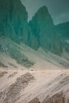 View of rugged, towering mountains rise majestically against a muted sky, casting long shadows across the textured, sandy terrain, Campitello di Fassa, Trentino-Alto Adige, Italy.