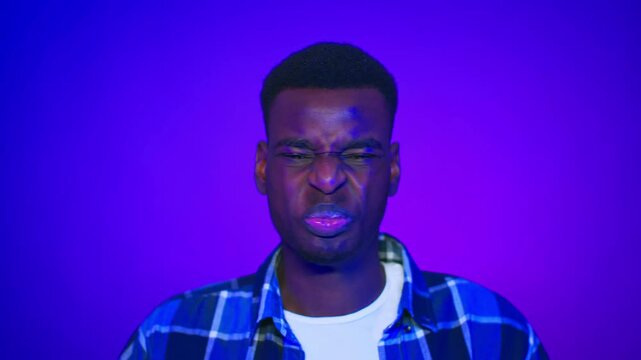 A young Black man is making a playful expression with his lips puckered and eyebrows raised. The background is bright purple, highlighting his features and expression.