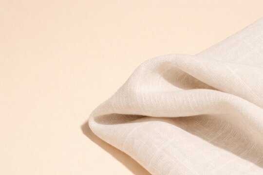 Close-up of gently draped white linen fabric on warm peach background with soft daylight, highlighting delicate texture, flowing folds, tactile comfort, and minimalist modern design.