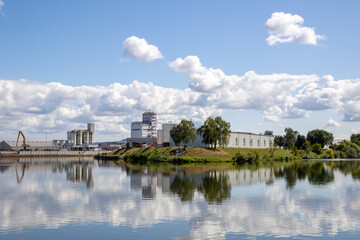 Naklejka premium Industrial riverside area in Bamberg, Bavaria, Germany, along the Regnitz River with boat tour activity, waterfront infrastructure and urban landscape mixed with surrounding natural scenery.