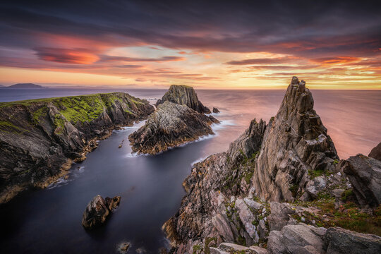 View of jagged cliffs meet the sea under a dramatic sunset sky, where vibrant colors paint the horizon in Malin Head, County Donegal, Ireland.