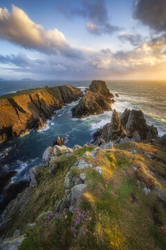 View of rugged cliffs meet the turbulent sea under a sky ablaze with warm sunset hues, creating a dramatic coastal vista, Malin Head, Ireland.