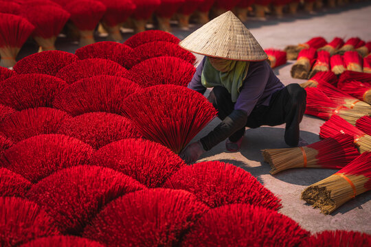 Aerial view of a woman in a conical hat arranging vibrant red incense sticks, creating a sea of color and texture, Ung Hoa, Ha Noi, Vietnam.