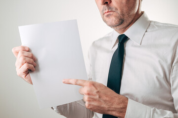 Serious businessman pointing at blank white paper sheet mockup