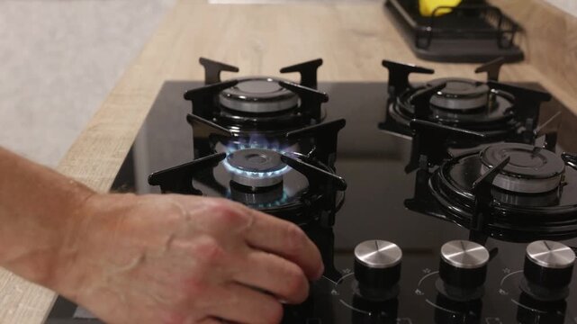 Close up of hand turning control knob on modern gas stove in kitchen, symbolizing cooking, household routine and domestic life.