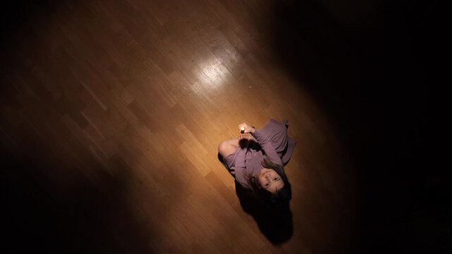 Young girl sitting alone on a wooden floor in a dimly lit room, holding a flickering candle, representing themes of loneliness, fear, and seeking comfort in darkness