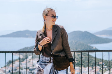 Travel blogger filming live stream on smartphone against mountain coastline, Gen Z female tourist on viewpoint, panoramic sea and hills, social media content creator, sunny outdoor vacation vibe. © shintartanya