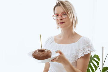 Pretty woman blowing candlelight on a chocolate donut, happy birthday celebration. 