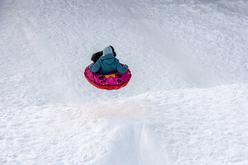 Child having fun on snow tube. Girl is riding a tubing, winter entertainment