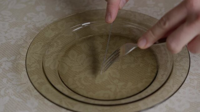 Close-up shot of a person scraping an empty plate with a fork and knife. Everyday dining sounds and gestures, finished meal moment and simple domestic routine at the kitchen table. High quality 4k