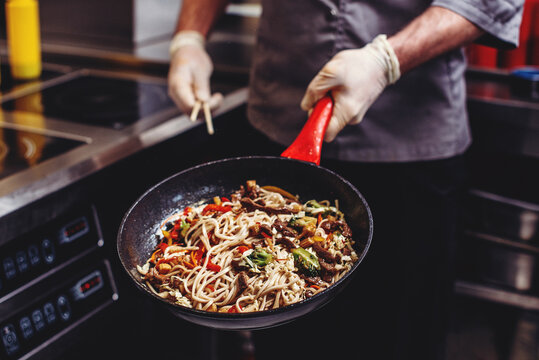 Wok noodles with vegetables being stir-fried in a hot pan in a restaurant kitchen. Asian cuisine cooking process close-up.