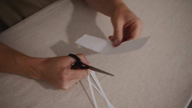 Male hands slowly cutting paper with scissors on a flat surface. Minimalistic home setting highlighting accuracy, control, and manual effort. High quality 4k footage