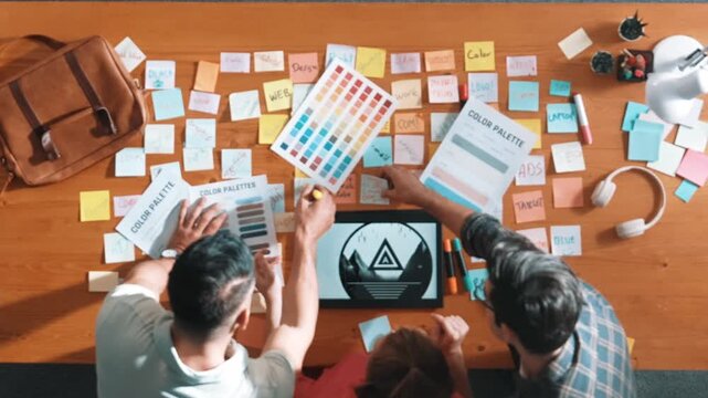 Top view of smart designer holding color palette while project manager looking at design and choosing color for program. Professional businesswoman taking a note while design creative logo. Symposium.