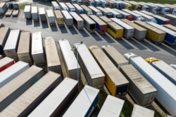 Blurred view of a large truck parking lot at a logistics hub, with multiple commercial semi trucks parked in organized rows