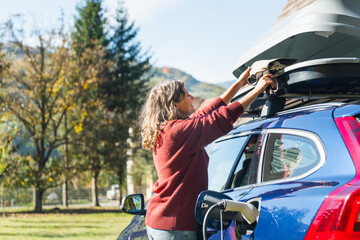 Woman traveler with backpack next to charging electric car