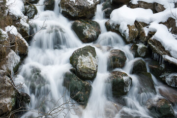 Water flowing over snow covered rocks in winter