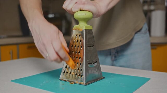 Medium shot of a man grating carrot while holding a kitchen grater by the handle. Stable food preparation process, simple home cooking and everyday kitchen routine. High quality 4k footage