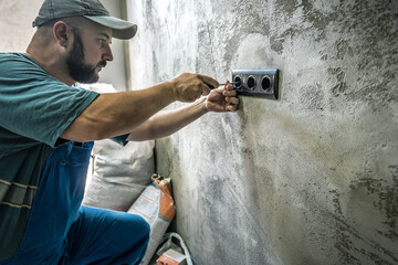 An electrician is installing black new sockets on the wall. Worker installing the power outlet
