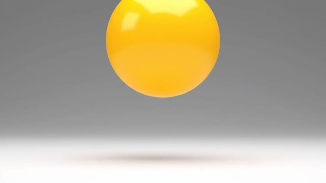 A bright yellow, reflective, egg-like sphere dynamically bounces and squishes on a neutral grey surface.