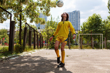 Teenage boy soccer player juggling ball during outdoor training on residential playground with city buildings and summer greenery