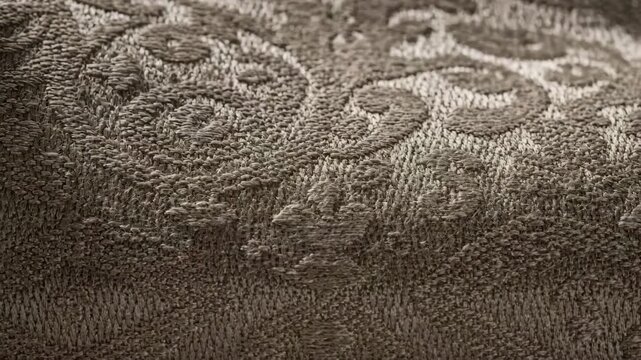 Closeup view of textured jacquard fabric highlighting raised damask patterns woven on an industrial loom perfect for elegant drapery designs.