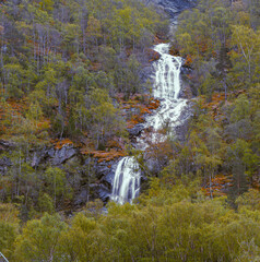 Tall Mountain Waterfall Flowing Through Forested Valley in Norway