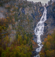 Tall Mountain Waterfall Flowing Through Forested Valley in Norway