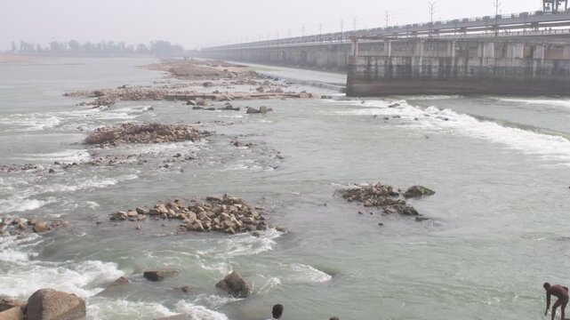 massive indrapuri barrage as it spans the son river, showing flowing water rushing past scattered boulders in a blend of nature and engineering