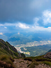 Fototapeta premium Mountain valley view toward Busteni Romania. Wide mountain valley view descending toward Busteni town beneath heavy clouds in Bucegi Mountains.
