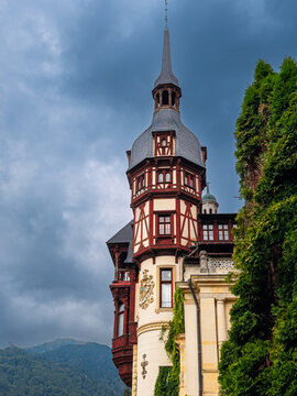 Peles Castle spire and facade. Tall spire and facade of Peles Castle framed by greenery and clouds