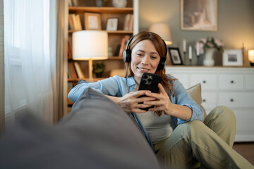 Obraz premium Woman relaxing at home, enjoying audio entertainment with smartphone and headphones