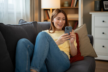Obraz premium Woman relaxing on sofa using smartphone browsing internet